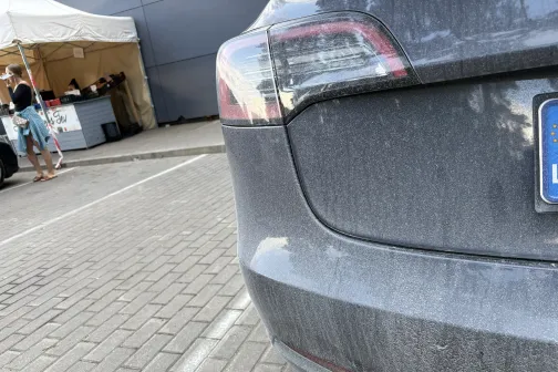 Netīrs pelēks auto stāvvietā.