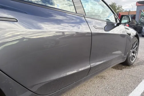 Pelēka automa&scaron;īna ar atspīdumiem uz sānu virsbūves.