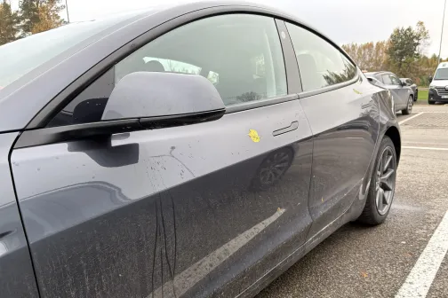 Netīrs pelēks automobilis stāvvietā.