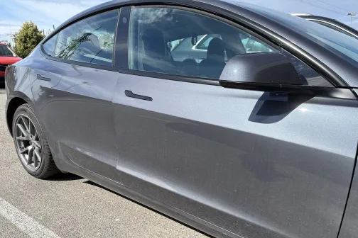 Netīrs pelēks auto saulainā dienā stāvvietā.