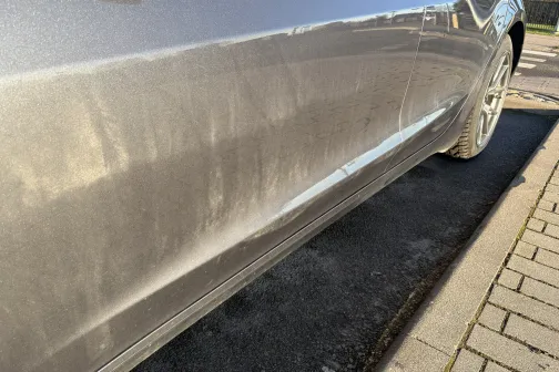 Netīrs sudrabains automa&scaron;īnas sāns, novietots uz ietves.