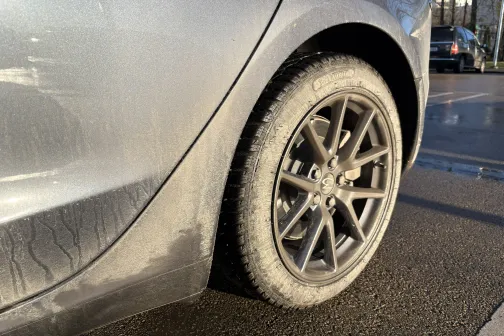 Netīrs sudraba auto aizmugurējais ritenis saulainā dienā.