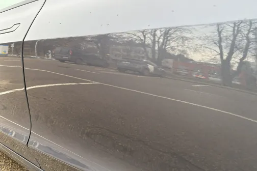 Spīdīgas automa&scaron;īnas durvis atspoguļo ceļu un kokus.