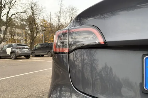 Pelēka automa&scaron;īna stāvvietā, fonā koki.