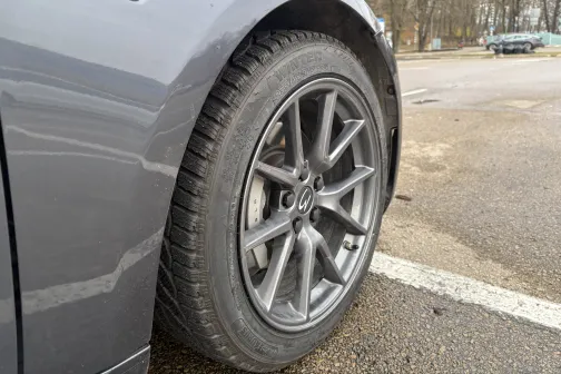 Pelēka automa&scaron;īna stāvlaukumā, redzams priek&scaron;ējais ritenis.