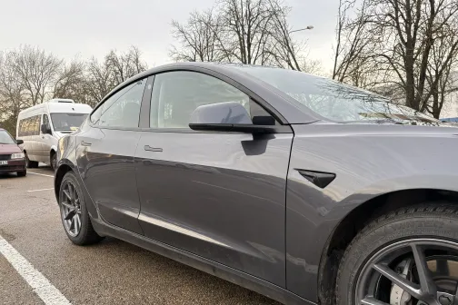 Pelēks automobilis novietots stāvvietā uz mitra asfalta.