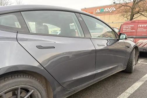 Tum&scaron;as automa&scaron;īnas sāns autostāvvietā, pelēkas debesis.