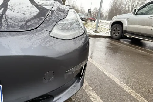 Pelēka automa&scaron;īna stāvvietā blakus citai automa&scaron;īnai, slapj&scaron; asfalts.