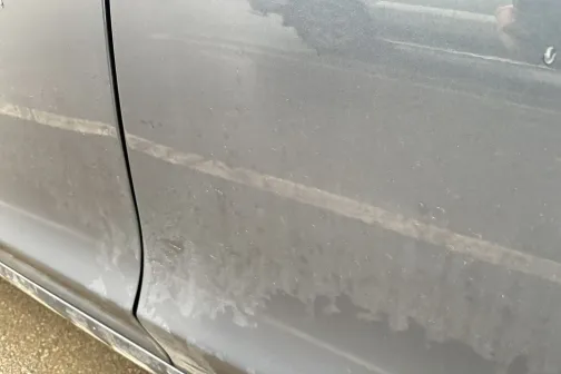 Netīrs pelēks auto sāns ar ceļa netīrumiem.