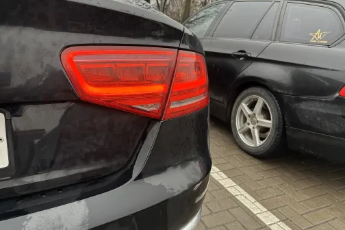 Divi auto stāvvietā, redzami aizmugurējie lukturi.