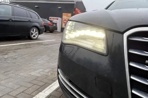 Automobiļa priek&scaron;ējais lukturis, kas spīd, stāvvietā.