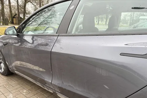 Netīrs sudrabkrāsas auto sānskats uz bruģētā laukuma.