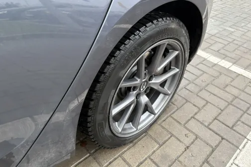 Pelēkas automa&scaron;īnas ritenis stāv uz bruģēta laukuma.