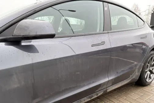 Netīrs pelēks automobilis stāvvietā, uz sānu durvīm redzami dubļi.