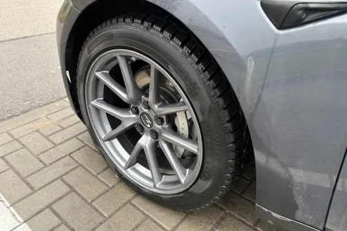 Pelēks auto ar tīru riteņa disku un riepu stāv uz bruģa.