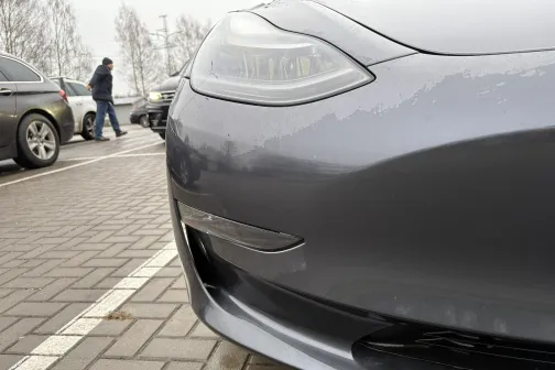 Sudraba automa&scaron;īnas priek&scaron;puse stāvlaukumā, fonā cilvēki.