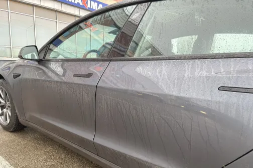 Netīrs pelēks auto stāvvietā pie ēkas.