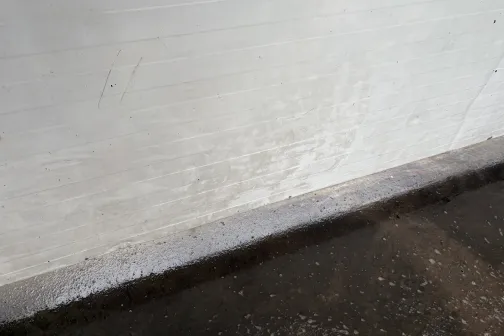 Balta netīra siena virs slapjas betona grīdas.