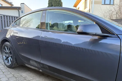 Netīrs melns auto pie privātmājas pagalma.