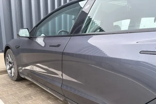 Sudraba auto sānskats pie metāla sienas.