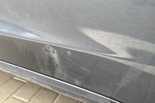 Netīrs pelēks auto sāns uz bruģa.