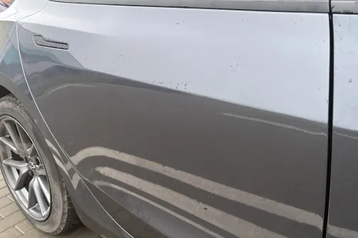 Pelēkas automa&scaron;īnas sānu durvis ar atspīdumiem.