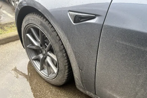 Netīrs pelēks auto ritenis uz slapja ceļa.