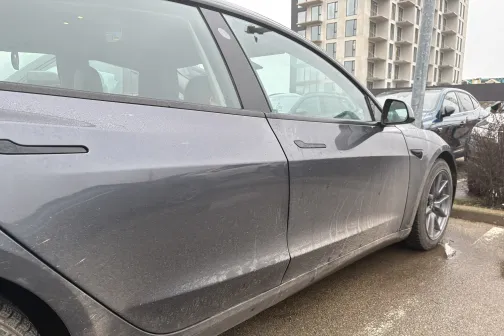 Netīrs pelēks auto stāvlaukumā pie ēkas.