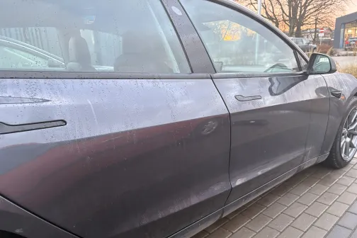 Netīrs pelēks auto novietots uz bruģa.