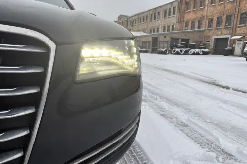 Auto priek&scaron;a ar ieslēgtu lukturi sniegotā pagalmā.