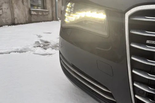 Automa&scaron;īnas priek&scaron;a uz ielas sniegā, ieslēgtas gaismas.