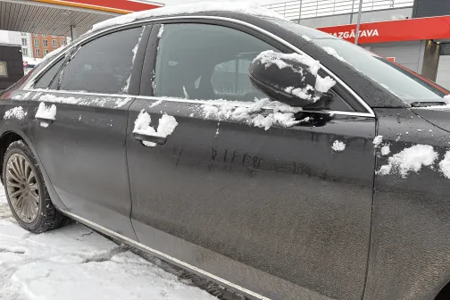 Netīra automa&scaron;īna ar sniega pārklājumu stāv pie auto mazgātavas.