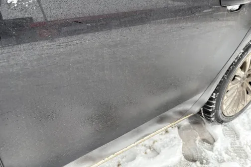 Netīra auto sānu durvis ar sniegu uz ceļa.