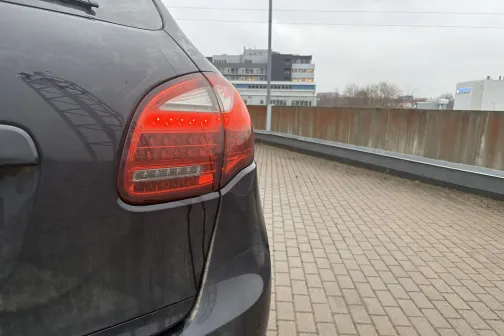 Netīrs automobilis ar ieslēgtām aizmugurējām gaismām stāvvietā.