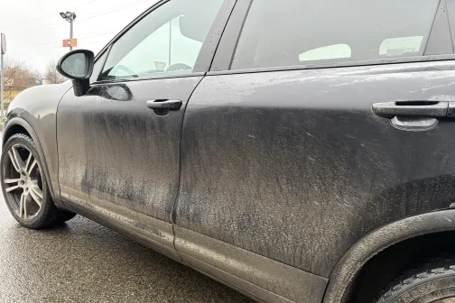 Netīrs melns auto uz ielas pēc lietus.