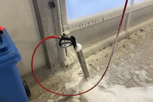 Austspiediena pistole automazgātavā ar sarkanu &scaron;ļūteni un ziepju putām uz grīdas.