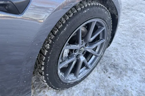 Pelēka auto riepa ar ziemas riepām sniegotā dienā.