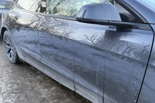 Netīra automa&scaron;īnas sānu daļa uz sniegota ceļa.