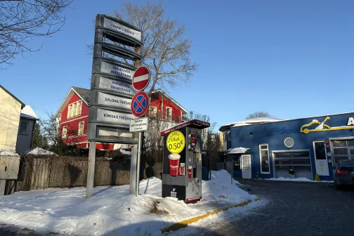 Auto mazgātava ziemā ar sniegu un ceļa zīmēm zem zilām debesīm.