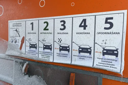 Mazgātuves instrukcija ar piecām darbībām uz oranžas sienas.