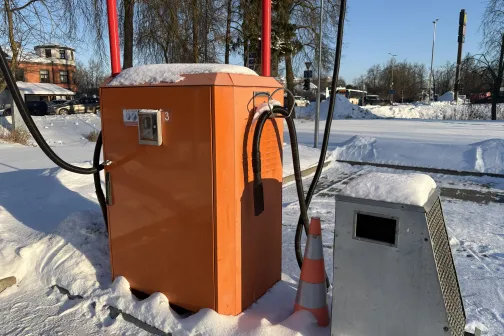 Oranžs putekļu sūcējs ziemas laikā ārpusē, apsnigu&scaron;i koki fonā.
