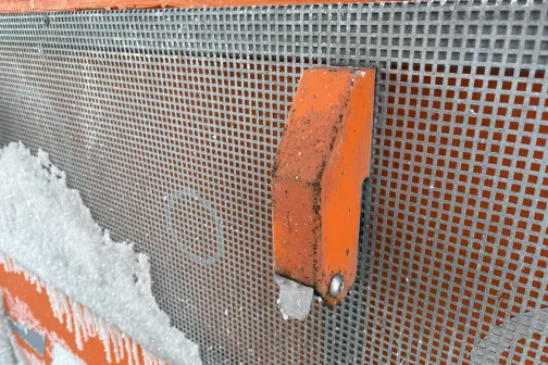 Metāla režģis ar oranžu elementu, klāts ledus kristāliem.