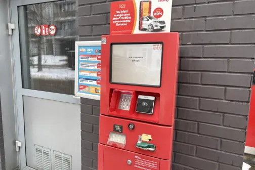 Sarkans automazgātavas maksājumu automāts pie pelēkas sienas.