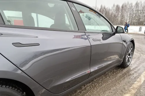 Pelēks auto, guļot novārtā netīrā ceļā, blakus redzams cilvēks.