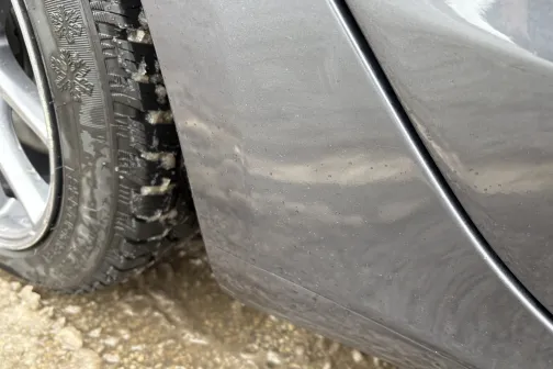 Auto sāna tuvplāns ar netīrumiem uz riepām un virsbūves.