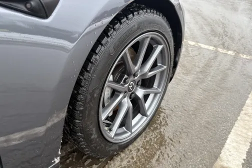 Pelēka auto ritenis ar slapju ceļu fonā.