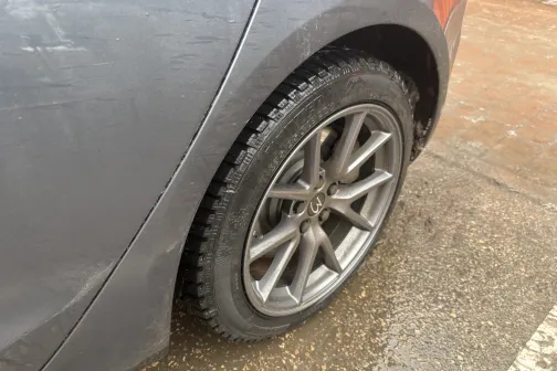 Pelēka auto aizmugurējais ritenis uz slapjas zemes.