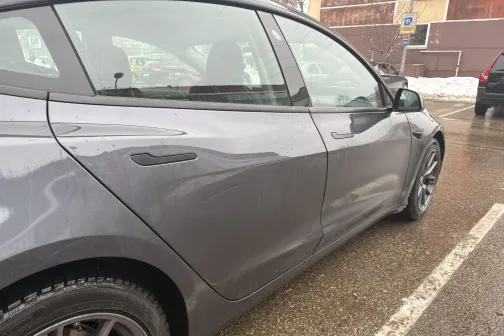 Pelēka automa&scaron;īna stāvvietā uz slapja asfalta.