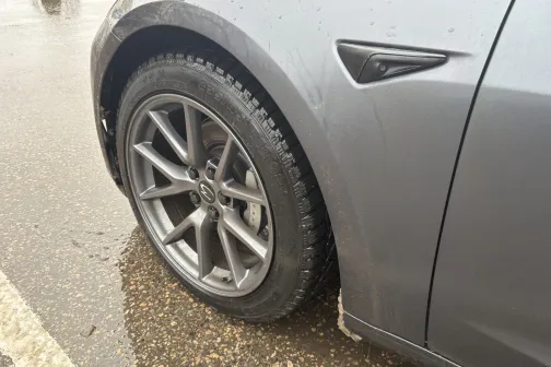 Pelēkas automa&scaron;īnas riepa un disks uz mitra ceļa.