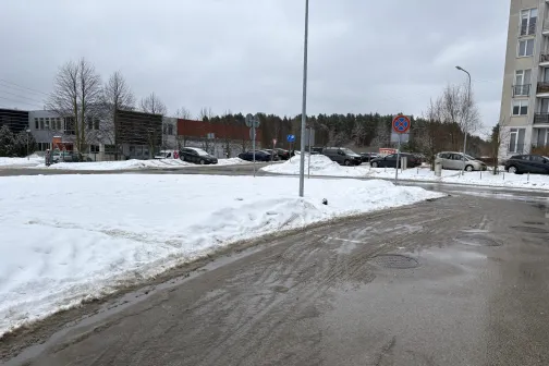 Sniegots ceļ&scaron; pilsētas teritorijā ar autostāvvietām fonā.